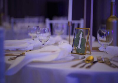 Festlich gedeckter Tisch mit weißen Servietten, Weingläsern, Besteck und einem Tischkartenhalter mit der Zahl '1'.
