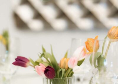 Glasvase mit bunten Tulpen in verschiedenen Farben auf einem festlich gedeckten Tisch im Festsaal.