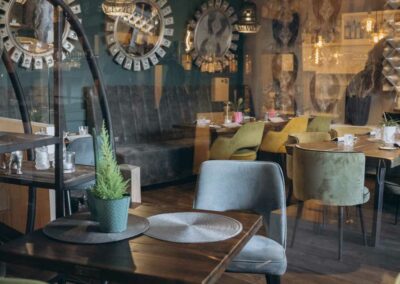 Gemütlicher Gastraum mit Holztischen, verschiedenen Stühlen und dekorativen Spiegeln an der Wand.