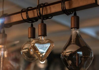 Drei hängende Glühbirnen mit schwarzem Kabel, darunter eine herzförmige, an einem horizontalen schwarzen Metallbalken.