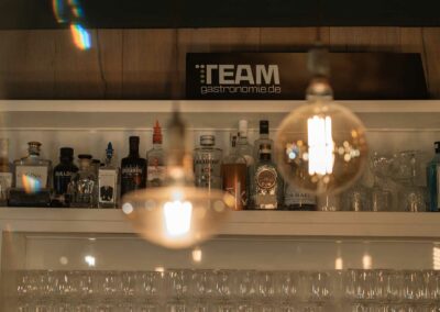 Regal mit verschiedenen Spirituosenflaschen und Gläsern, darüber ein Schild mit der Aufschrift 'TEAM gastronomie.de'.